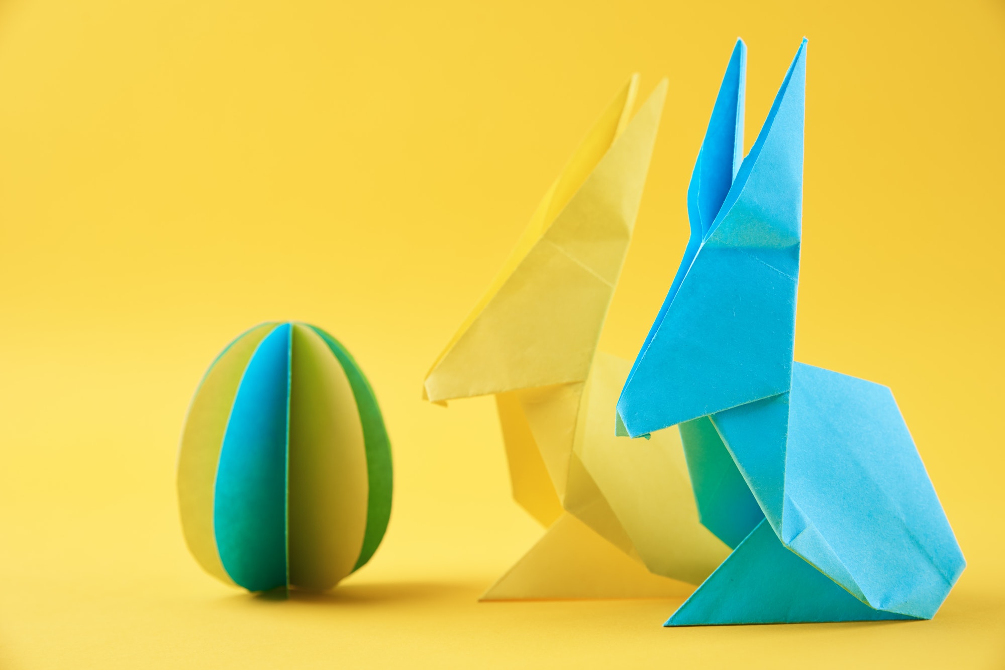 two paper origami esater rabbits and colored egg on yellow background easter celebration concept